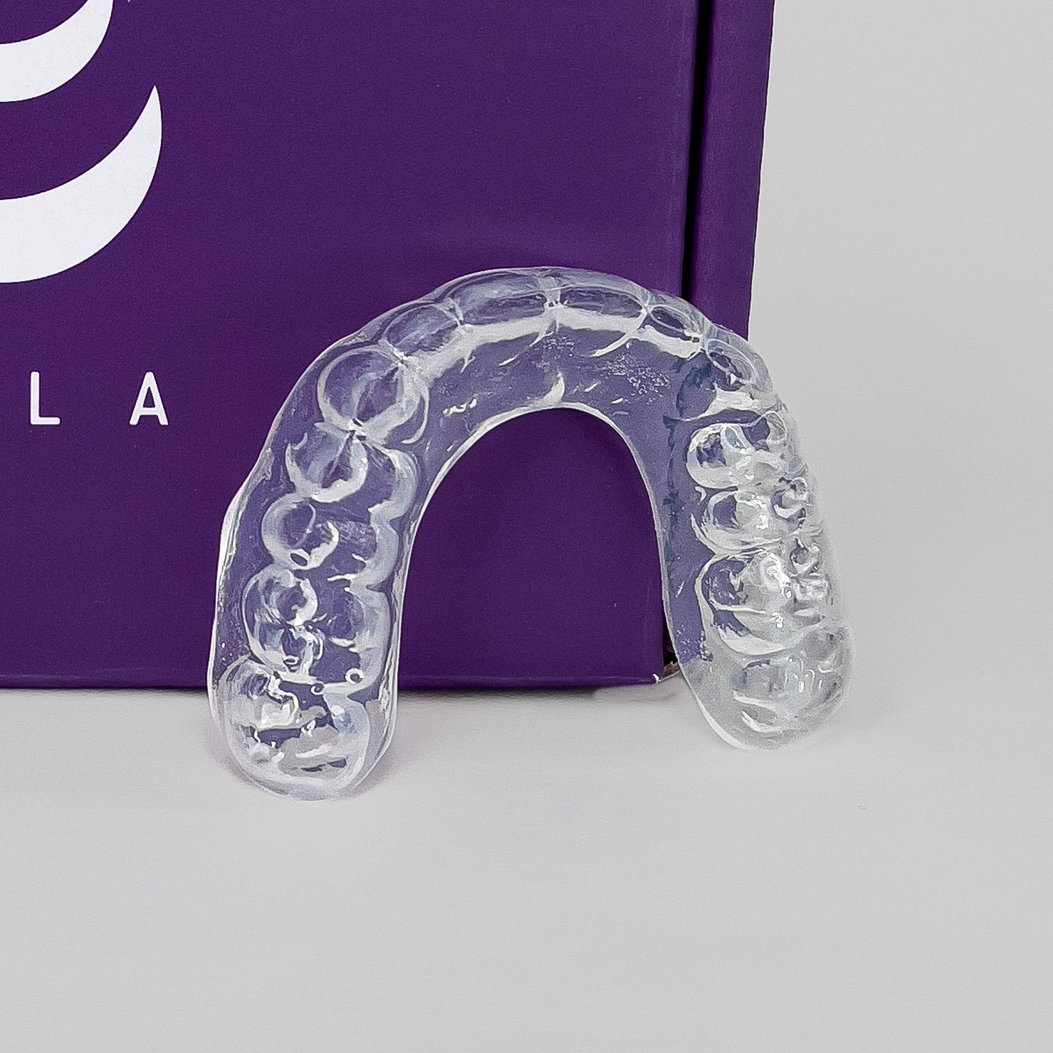 Clear sports mouthguard in front of a purple Lyla box on a gray background