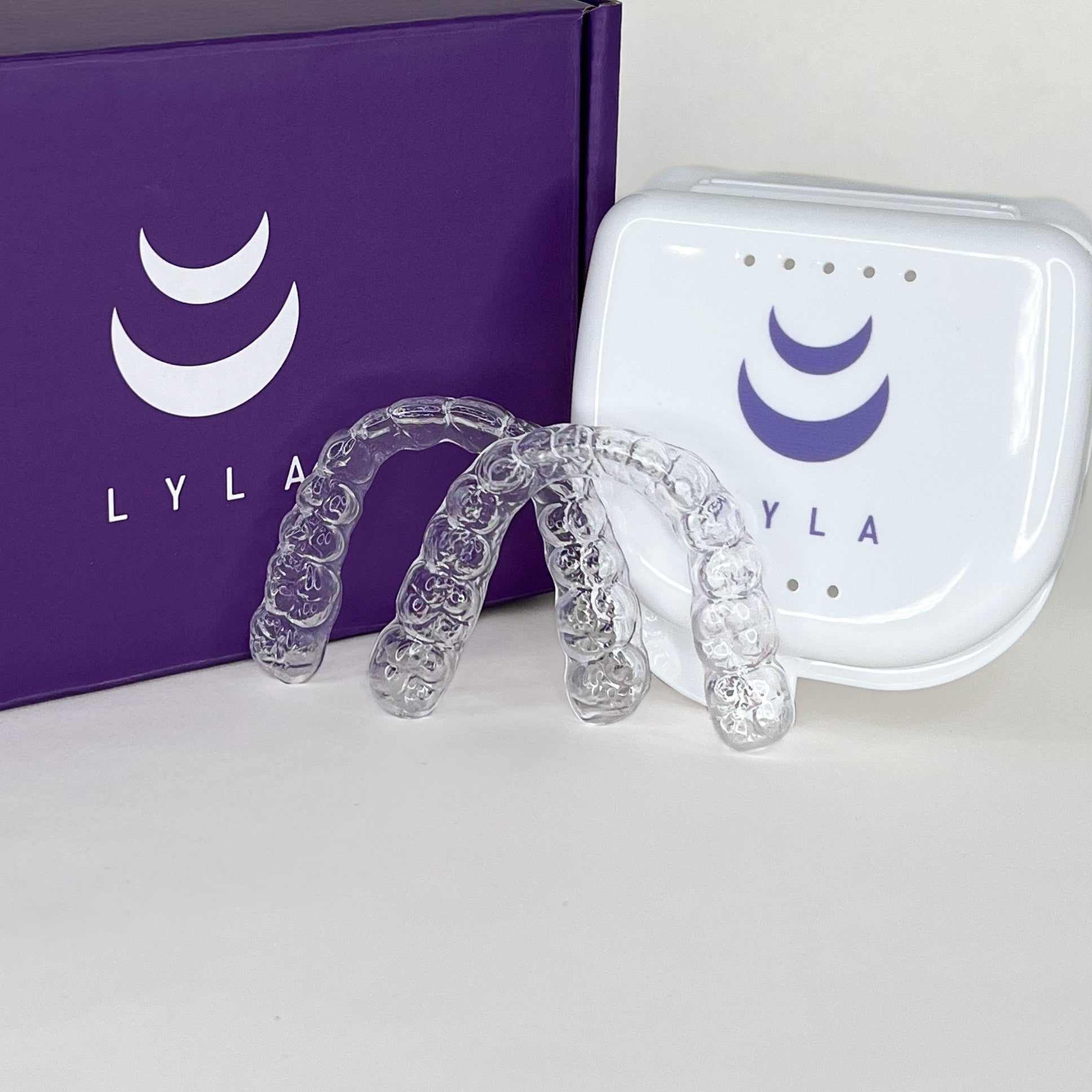 Clear aligners with a white case on a purple Lyla box.