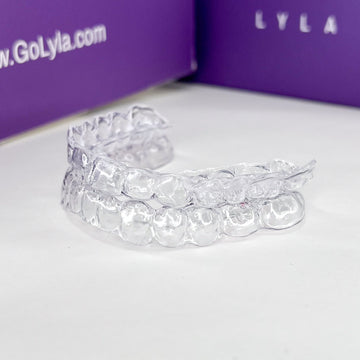 Clear dental aligners on a white surface with a purple Lyla box in the background.