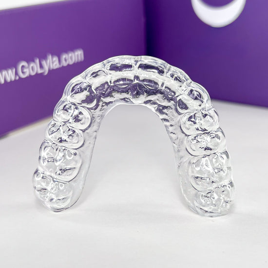 Clear aligner tray on a white surface with a purple box in the background displaying 'www.GoLyla.com'.